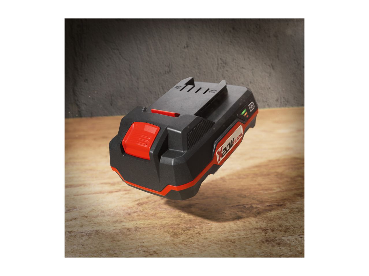 A black and red power tool battery with a charge indicator, floating above a wooden surface.