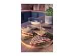 Grilled sandwiches with prosciutto, mozzarella, tomato, and arugula on a wooden board in a kitchen.