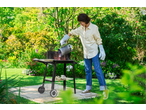 Grillmeister Trolley Barbecue with a woman adding charcoal in a lush garden.