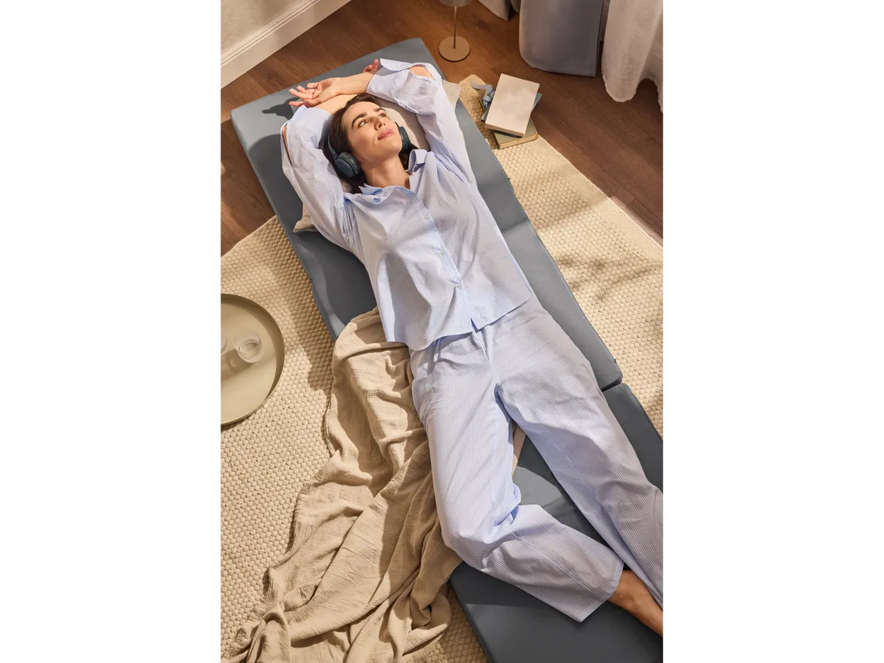 Una donna in pigiama a righe blu e bianche sdraiata su un materasso grigio con le cuffie.