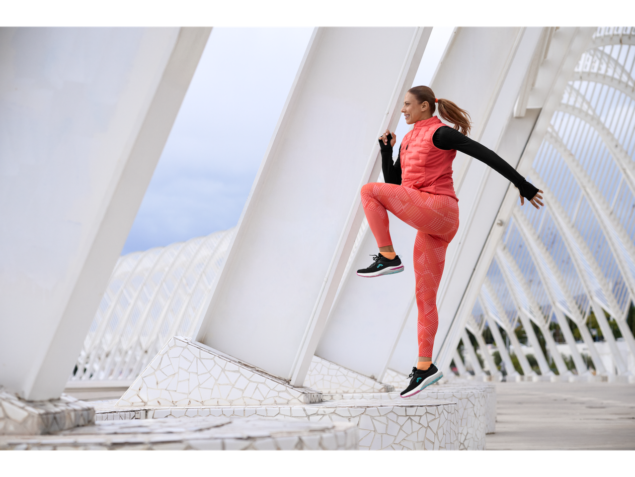 Mulher com colete de treino coral e leggings estampadas, a exercitar-se ao ar livre.
