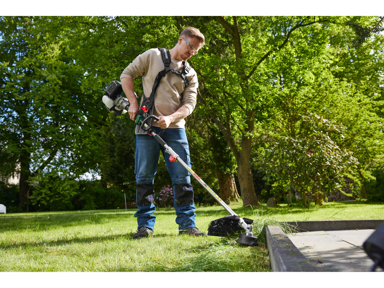 Bărbat folosind un aparat combinat pe benzină PARKSIDE® 4-în-1 pentru a tunde iarba în grădină.
