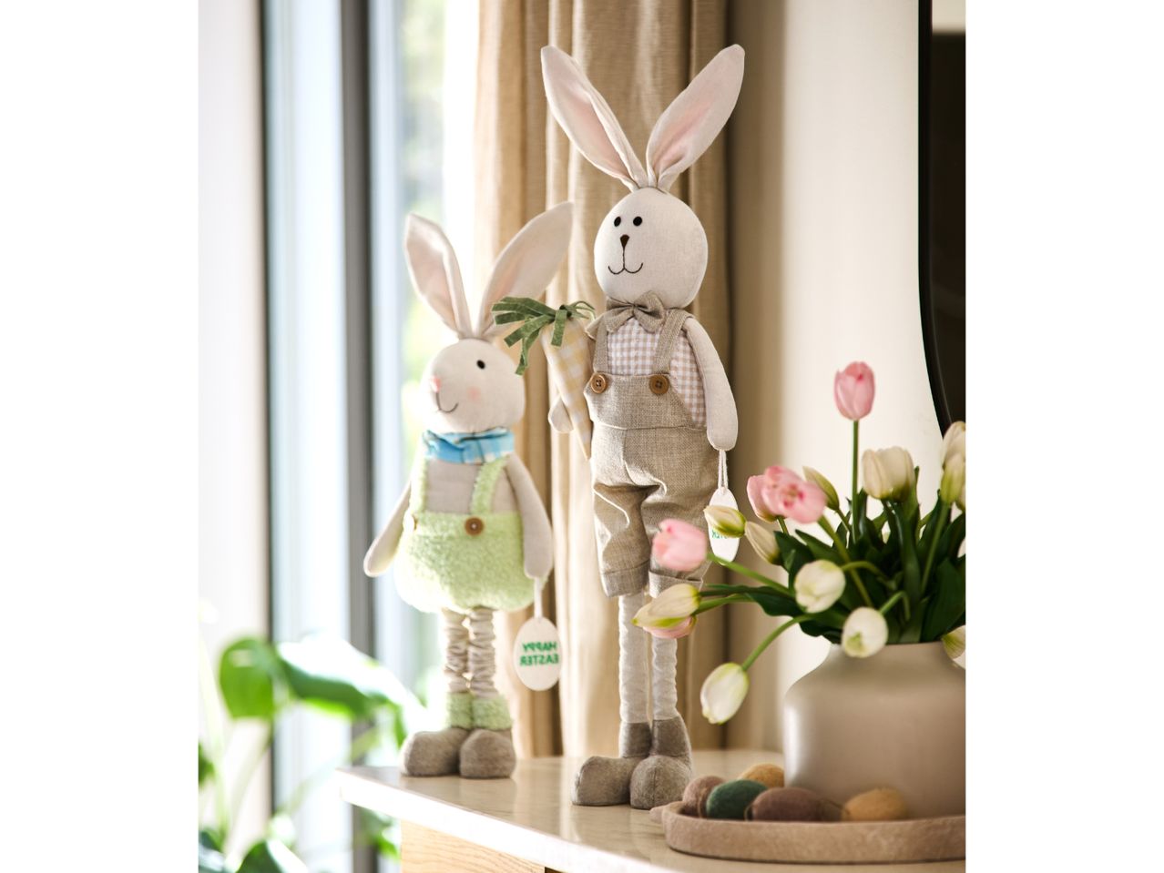 Two Easter bunny plush toys, one holding a carrot, with tulips and decorative eggs.