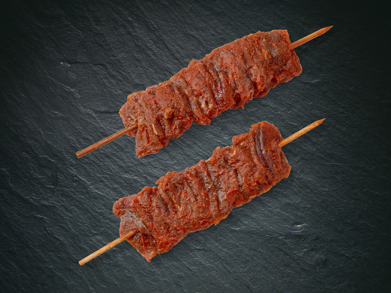 Deux brochettes de viande grillée sur une surface sombre.
