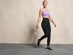 Woman in a purple sports bra and black leggings holding a water bottle.