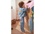 Child in Mickey Mouse denim jacket and jeans drawing on a cardboard playhouse.