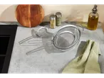 Kitchen counter with stainless steel strainers, cutting board, spice jars, and oil bottle.