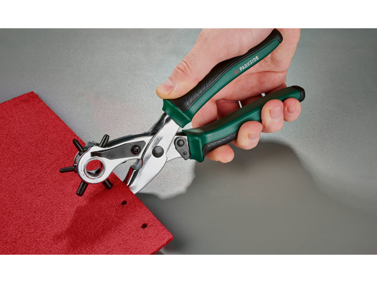 Ruka koristi klešta za bušenje rupa na komadu crvenog materijala.