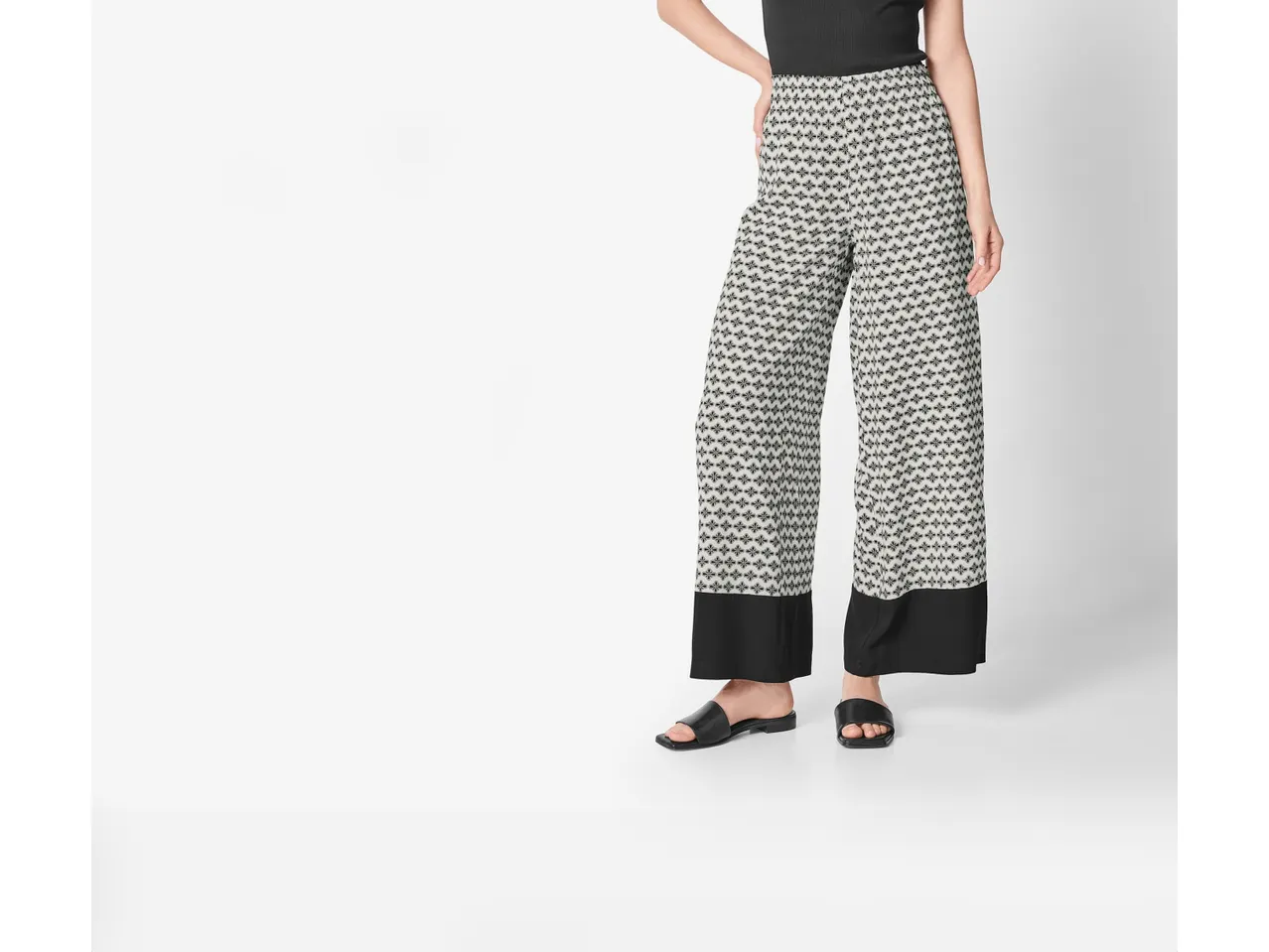 Pantaloni palazzo a stampa geometrica con fondo nero e sandali piatti.