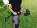Person holding a green and black electric grass trimmer with an orange cable in a garden.
