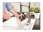 Man rinsing a dark sponge under a modern kitchen faucet in a white sink.