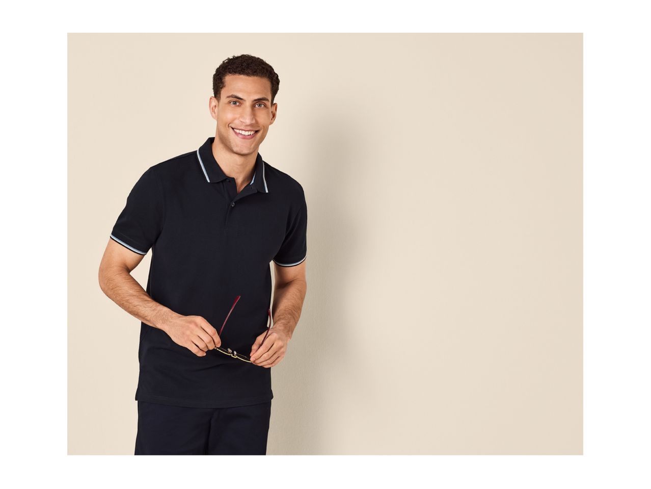 Man in a navy polo shirt with light blue and white striped trim, holding glasses.