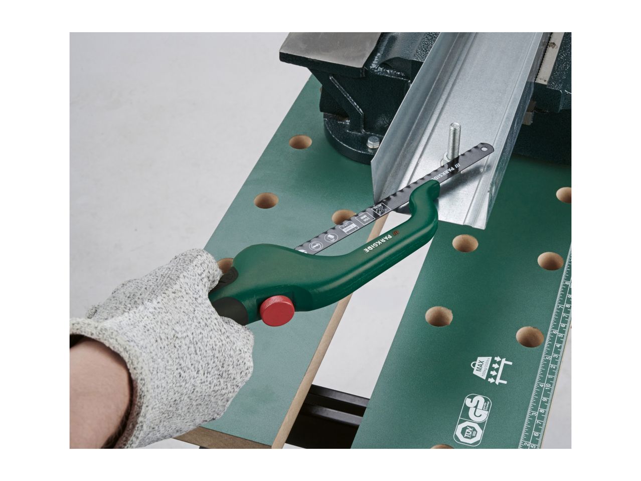 A person wearing a glove uses a hacksaw to cut a metal profile on a workbench.