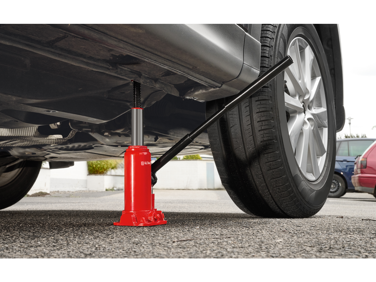 Red hydraulic bottle jack lifting a car, with a tire and wheel visible.