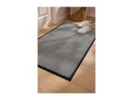 Grey striped doormat with a black border on a wooden floor next to white sneakers.