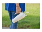 Woman in blue top and jeans holding a white travel mug with a straw.