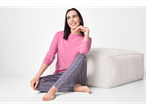 Vrouw in roze en bloemen Esmara pyjama, zittend op een witte poef.