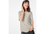 Smiling woman in a light grey t-shirt and dark jeans, wearing gold earrings and a bracelet.