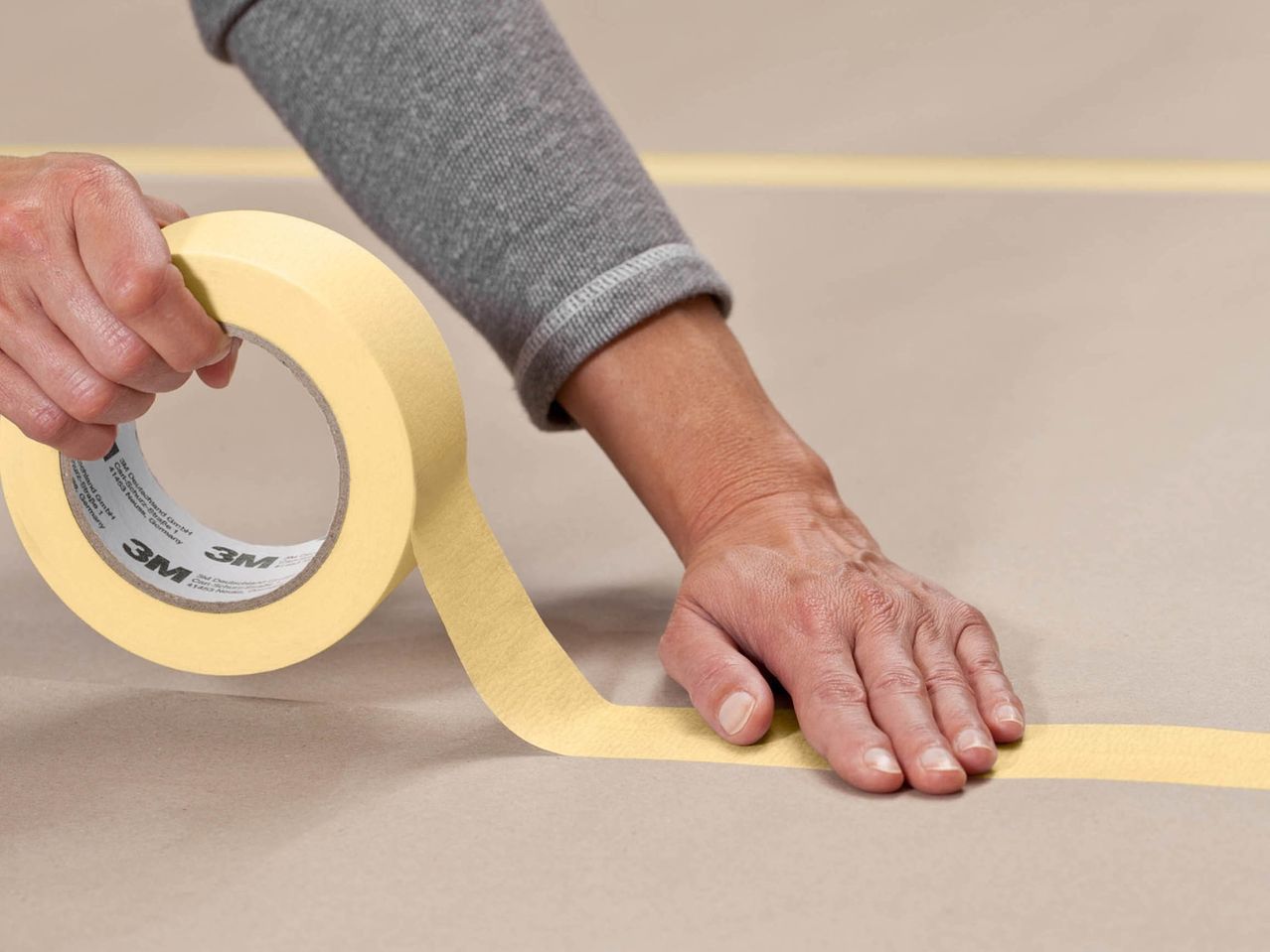 A person applying 3M masking tape to a surface.