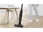 Cordless 2-in-1 vacuum cleaner on a light wooden floor next to a person's legs.