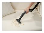 Handheld vacuum cleaner attachment cleaning crumbs off a beige sofa