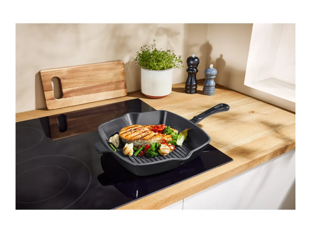 Grilled salmon and vegetables in a cast iron pan on an induction cooktop.