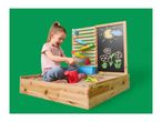 Child playing in a wooden sandbox with a water wall and chalkboard drawing of sun and flowers.