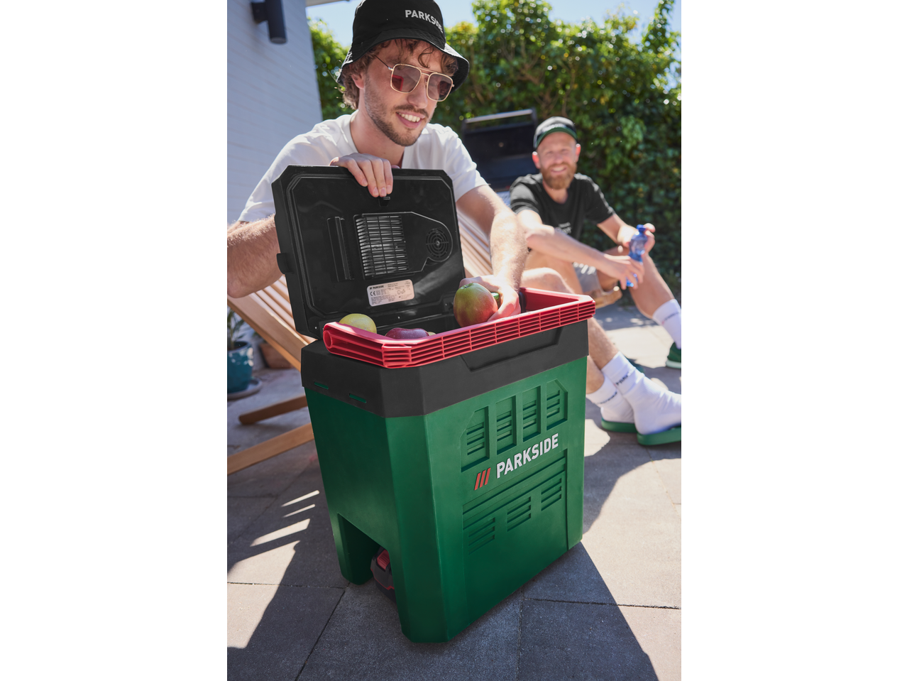 Bărbat deschizând o ladă frigorifică PARKSIDE cu fructe, un alt bărbat în fundal.