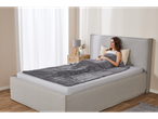 Relaxed woman on bed, covered with a gray blanket.
