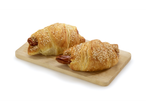 Deux croissants aux saucisses avec des graines de sésame sur une planche à découper en bois.