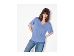 Woman in a blue V-neck t-shirt and jeans, leaning against a white wall.