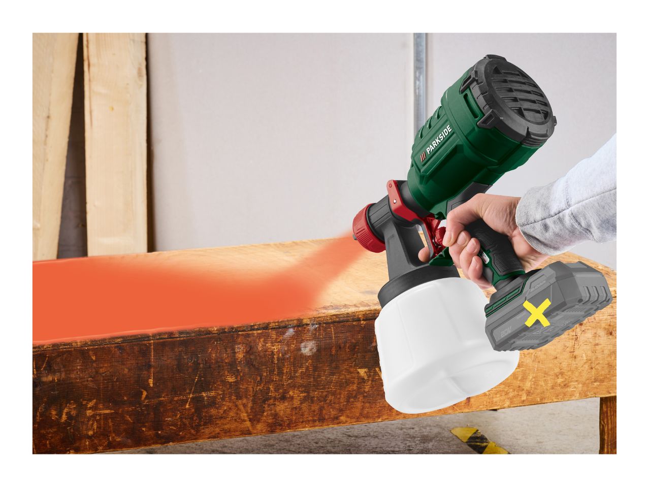 A person spray painting a wooden surface with an electric paint sprayer.