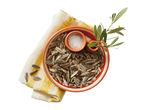 Sunflower seeds in a bowl with salt and an olive branch on a striped napkin.