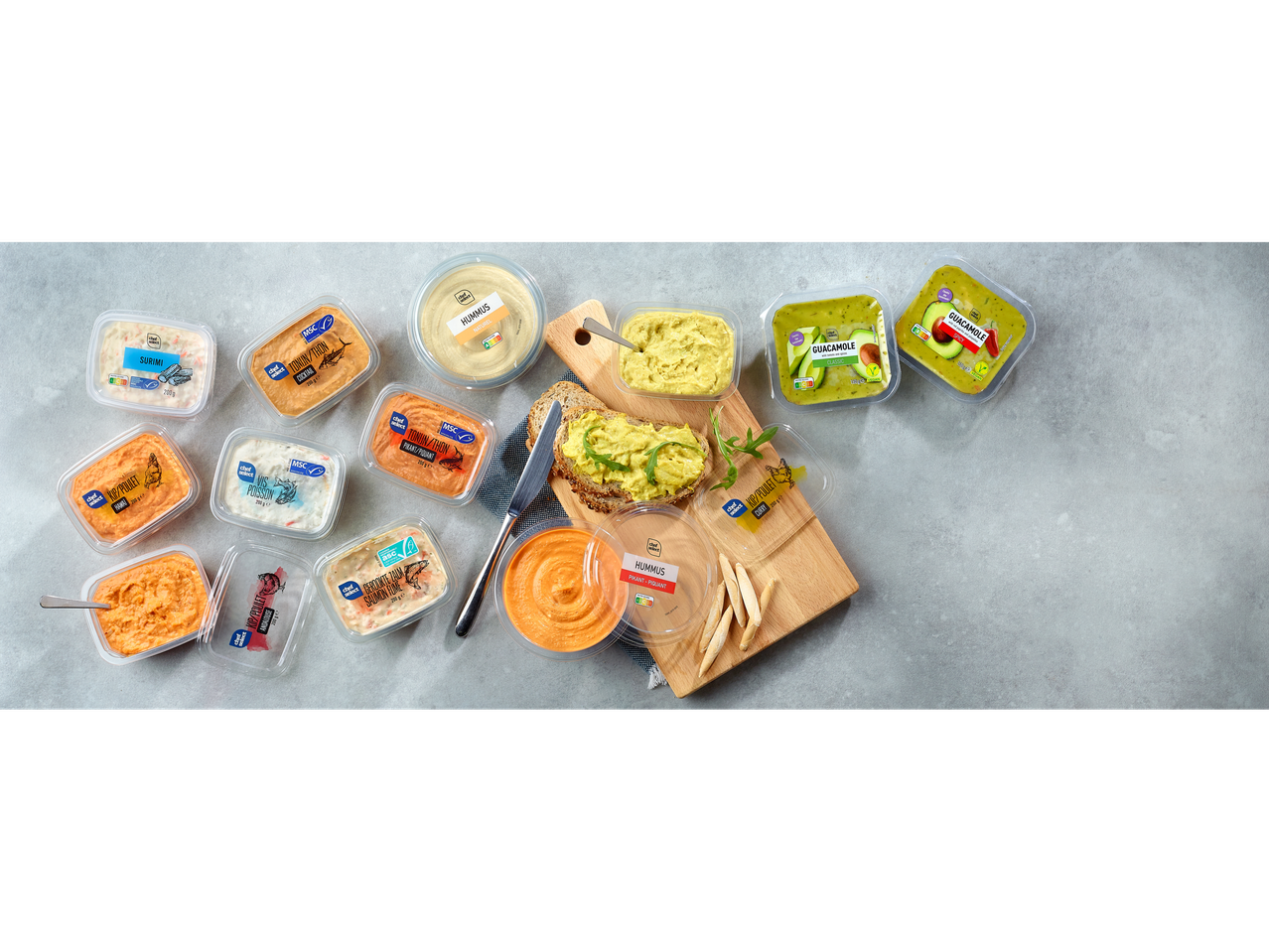 Houmous, guacamole et diverses pâtes à tartiner Chef Select sur une surface grise avec du pain et des craquelins.