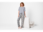 Woman in grey t-shirt and patterned pajama pants, leaning on a white chair.