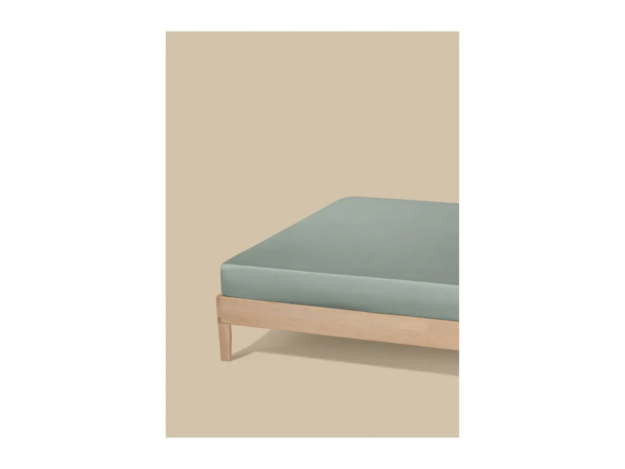 Light green fitted sheet on a wooden bed frame against a beige background.