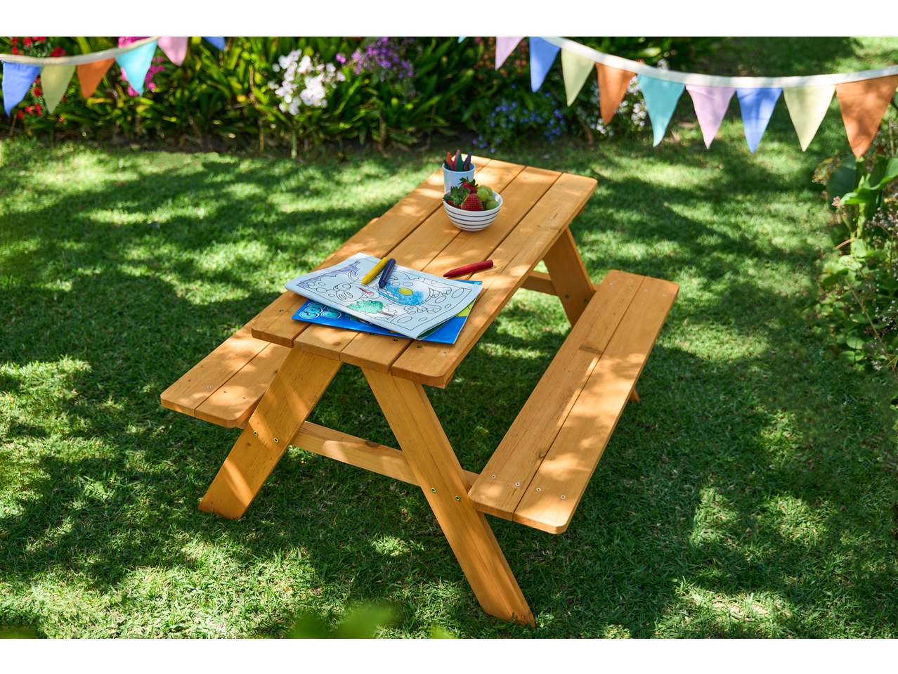 Livarno Kids' Bench with coloring book and fruit in a sunny garden with bunting.