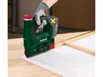 Uma pessoa com luvas usa um agrafador elétrico verde e vermelho para prender uma tela a uma moldura de madeira.