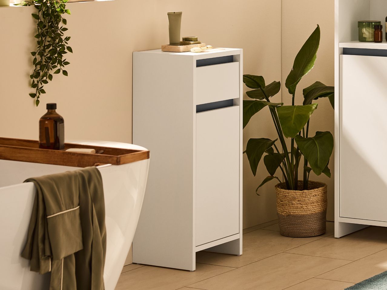 Bathroom with a white tall cabinet, bathtub with wooden tray, and a large potted plant.