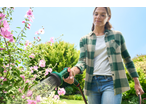 Woman watering pink flowers with a garden hose and spray gun.