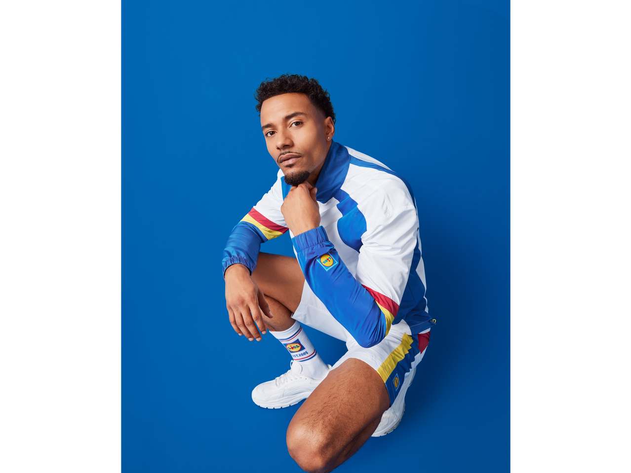 Man in a white, blue, red, and yellow tracksuit with matching socks and white sneakers.