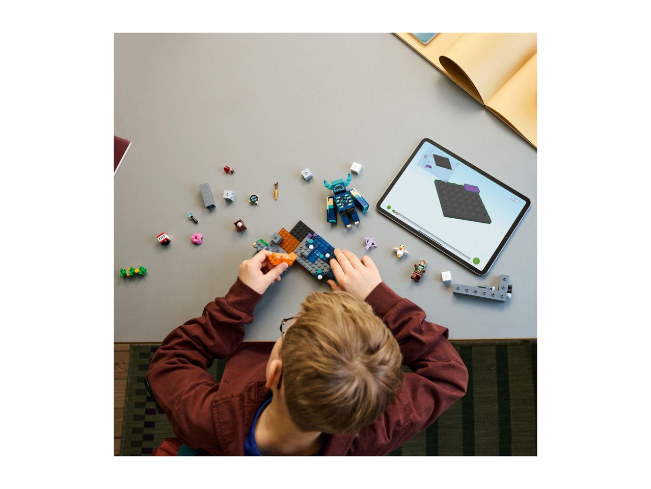 Overhead view of a child building a toy set on a table, with a tablet displaying instructions.