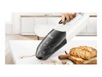 A Bosch hand-held vacuum cleaner cleans crumbs from a kitchen table near a loaf of bread.