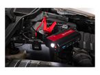 Portable jump starter with clamps connected to a car battery in an engine bay.