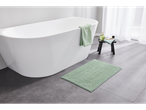 White bathtub with a green bath mat and towel in a modern bathroom.