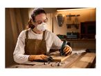 Woman in safety gear using a rotary tool to engrave wood, with various bits on the workbench.