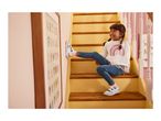 A child in a white rainbow sweatshirt and blue jeans sits on wooden stairs, wearing white and blue sneakers.