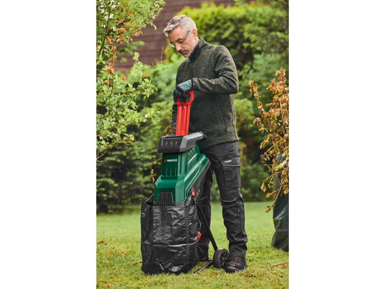 Homem usando um triturador de jardim Parkside para processar galhos no gramado.