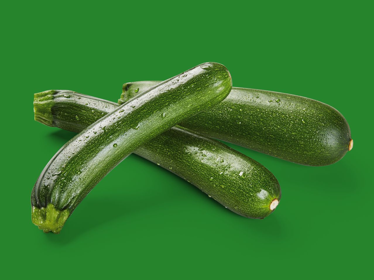Drei frische Zucchini mit Wassertropfen vor grünem Hintergrund.