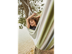 Woman relaxing in a striped hammock by the water.